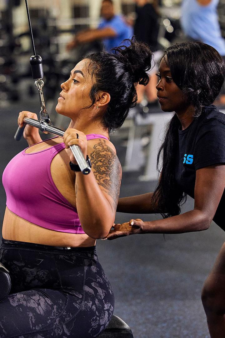 Personal trainer assisting a woman with a lat pulldown exercise in the gym