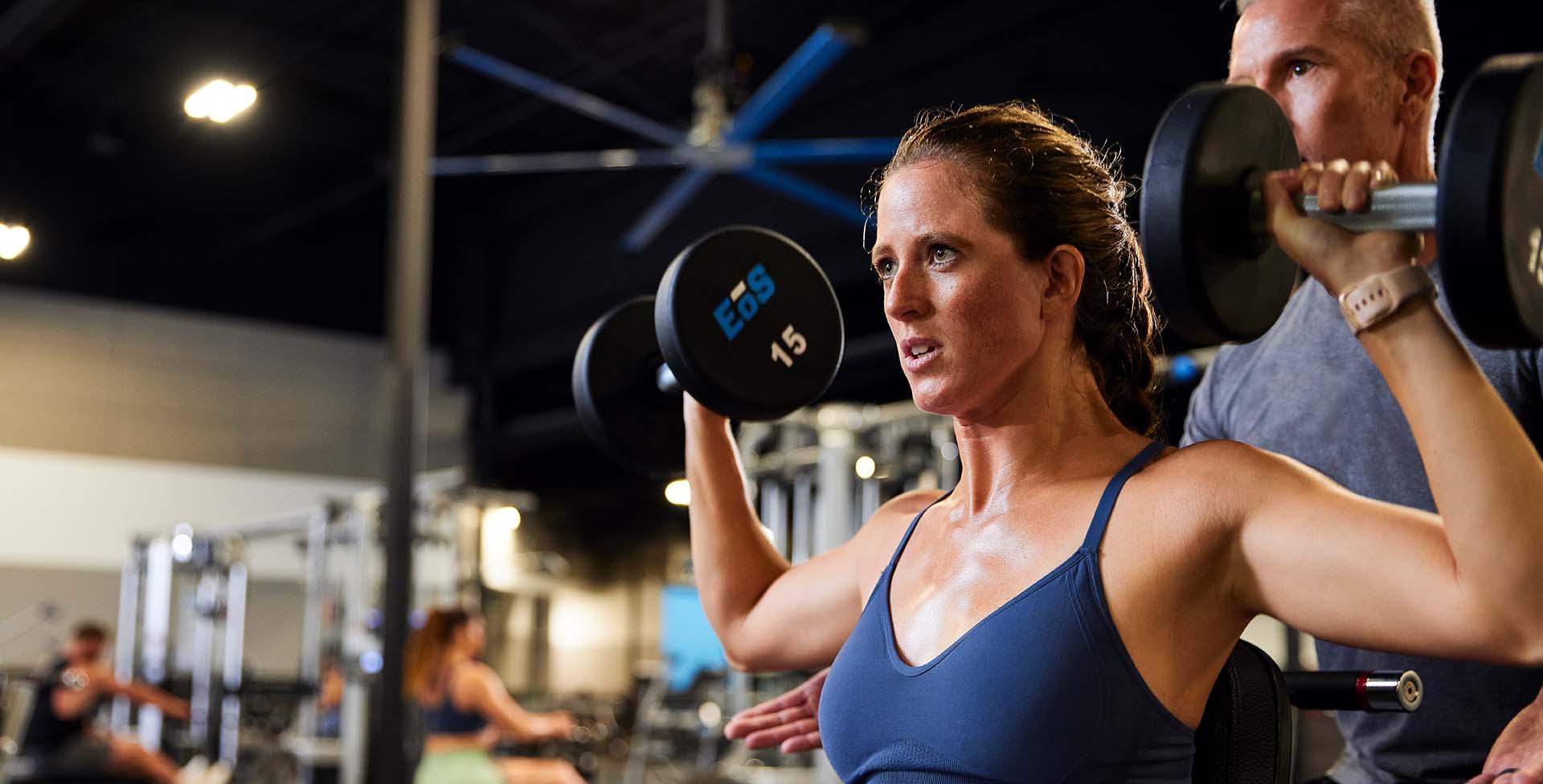 eos gym member doing an shoulder press with two dumbbells