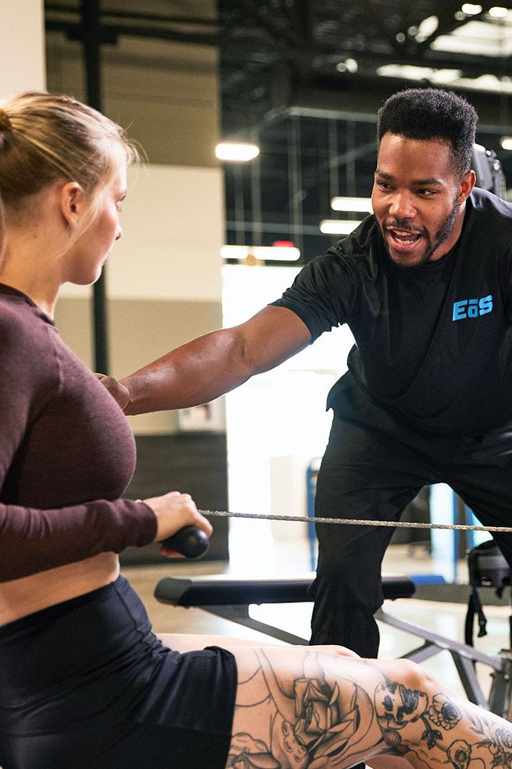 Personal trainer giving guidance to a woman on a rowing machine in a gym