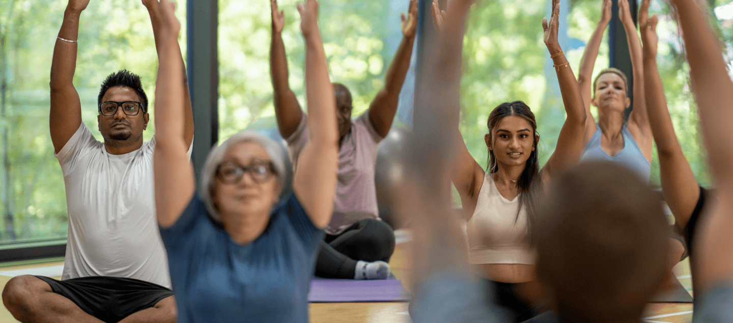 A group of people in a fitness class, raising their arms during a stretching exercise