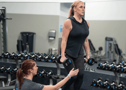 Trainer assisting woman with a weighted exercise in the gym