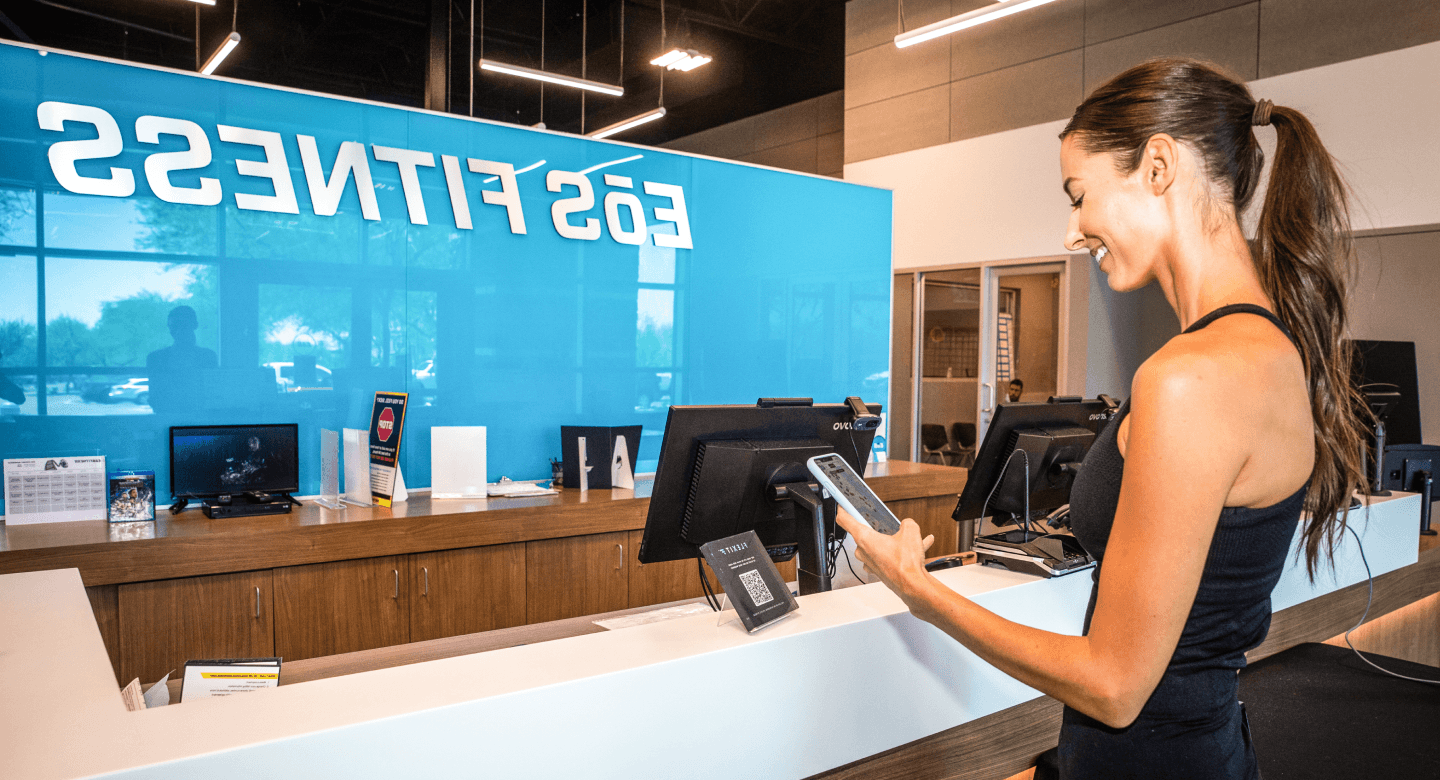 A woman smiling while using her smartphone at the front desk of a gym