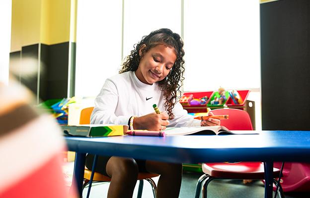 young child drawing on a classroom table