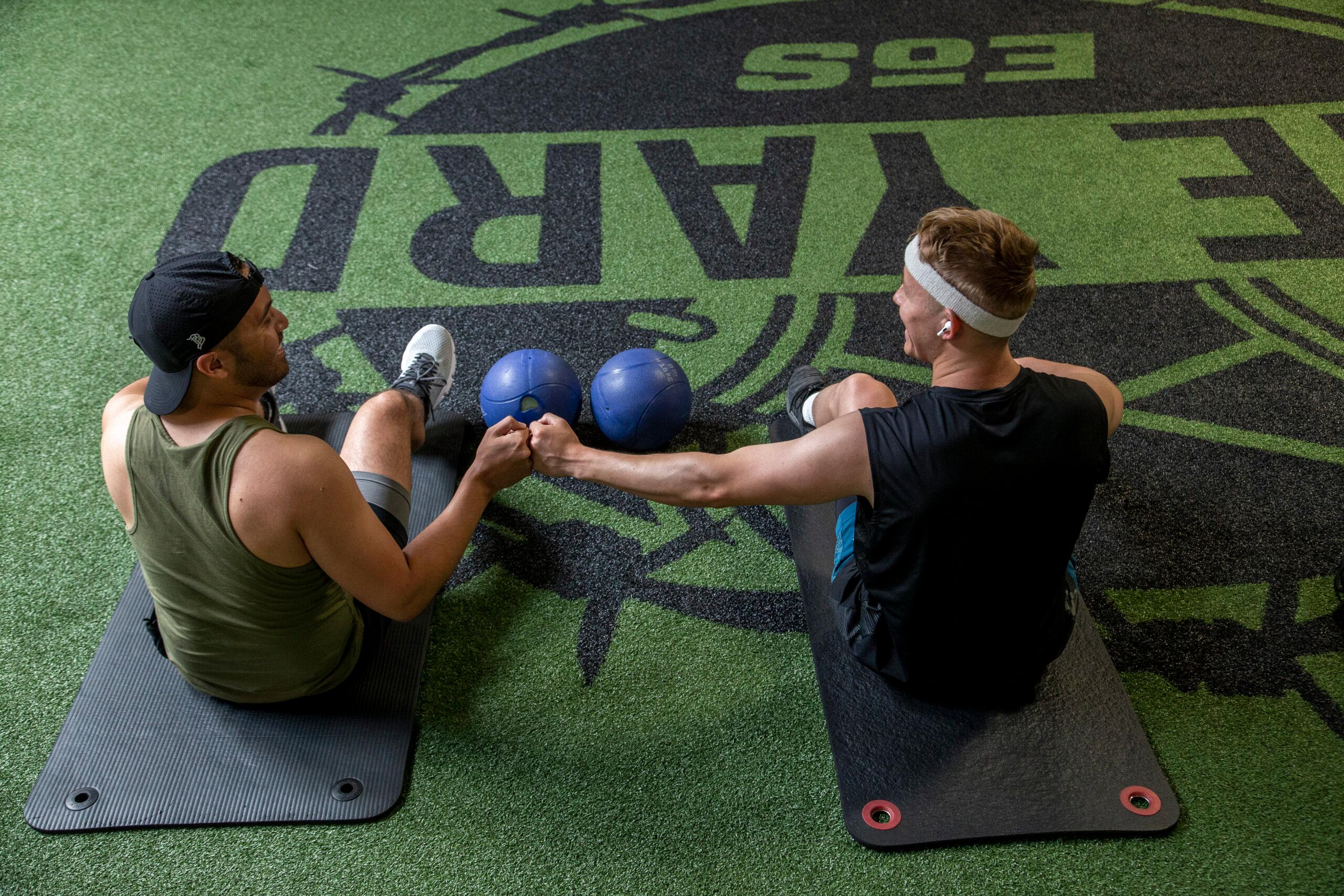 two eos gym members sitting on indoor turf fist bumping