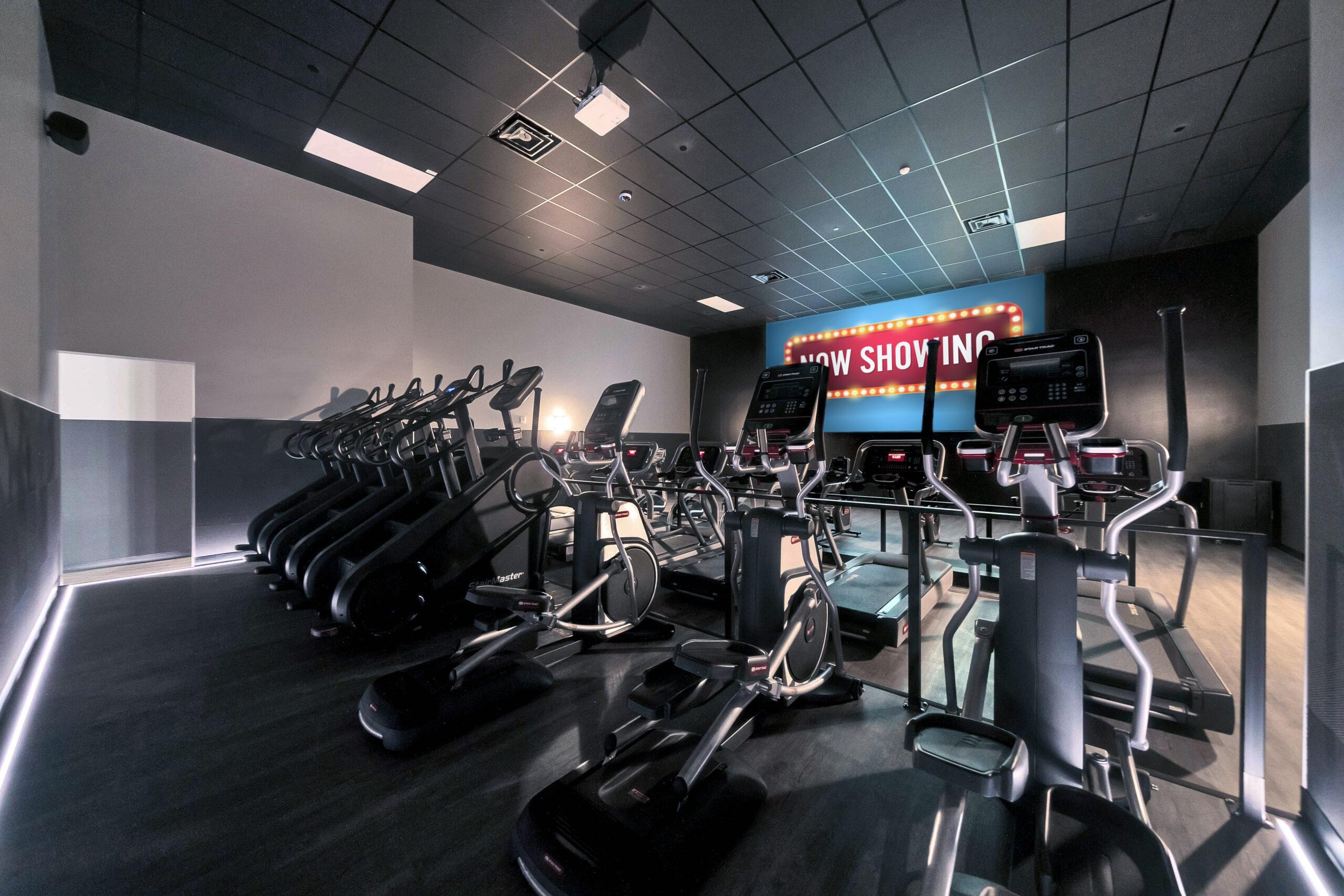 cinema room full of different cardio equipment and a large screen