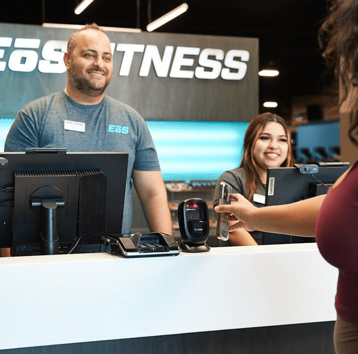 two smiling staff members helping an eos gym goer check in