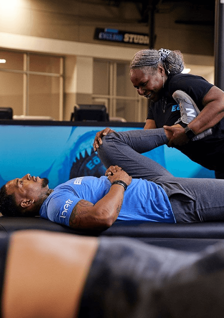 eos gym member getting leg stretched on table by personal trainer