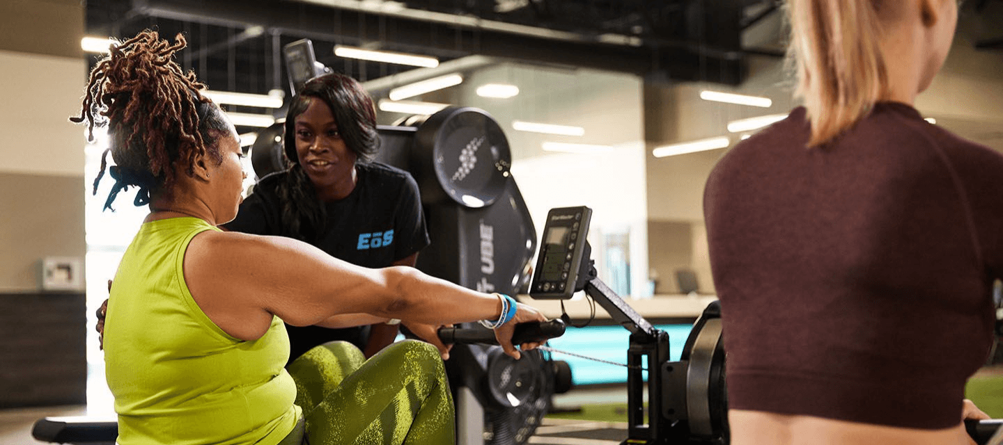 Gym trainer assisting a client on a rowing machine