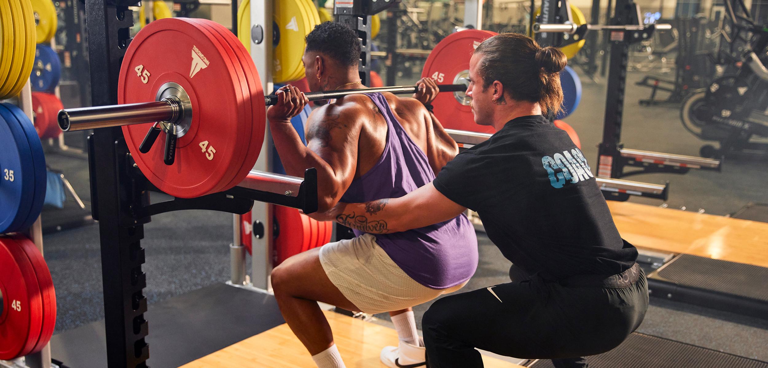 eos coach spotting athletic eos gym member on barbell squat