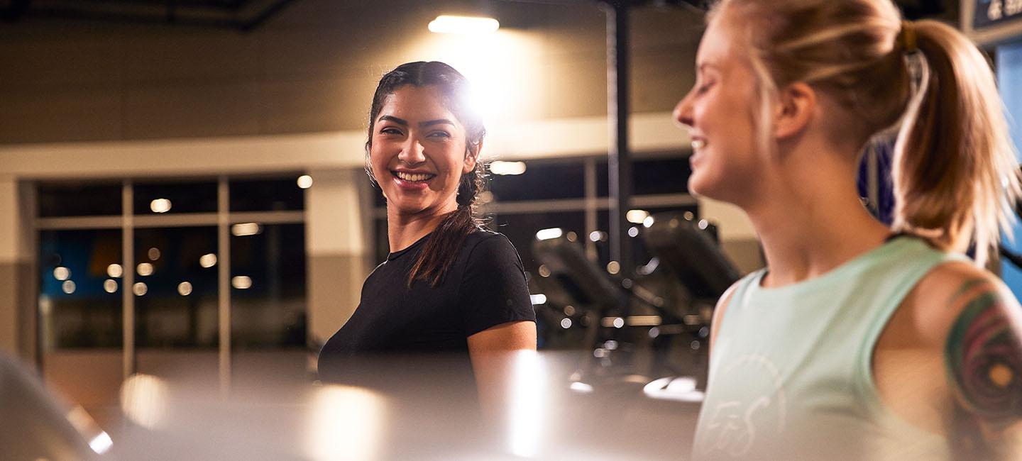 two eos gym members smiling at each other on cardio equipment