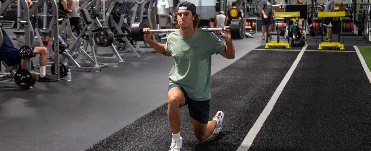 eos gym member doing barbell lunges on turf