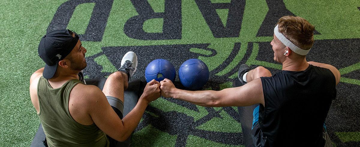 two eos gym members smiling and fit bumping after a workout 