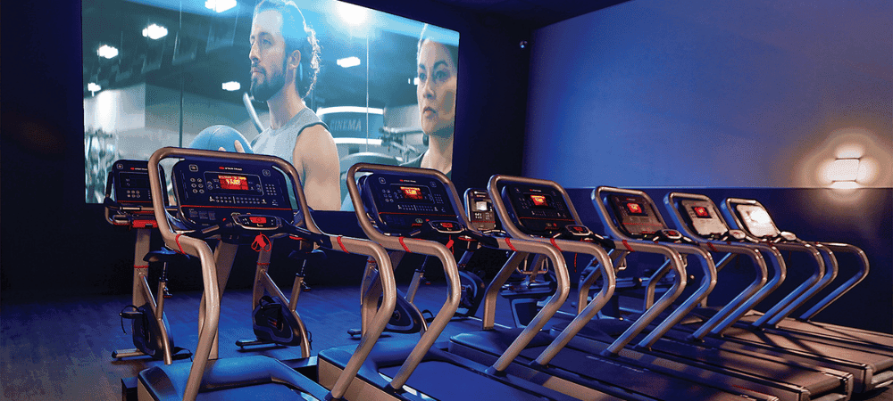 cardio equipment lined up to a cinema screen at a EōS Fitness San Diego gym