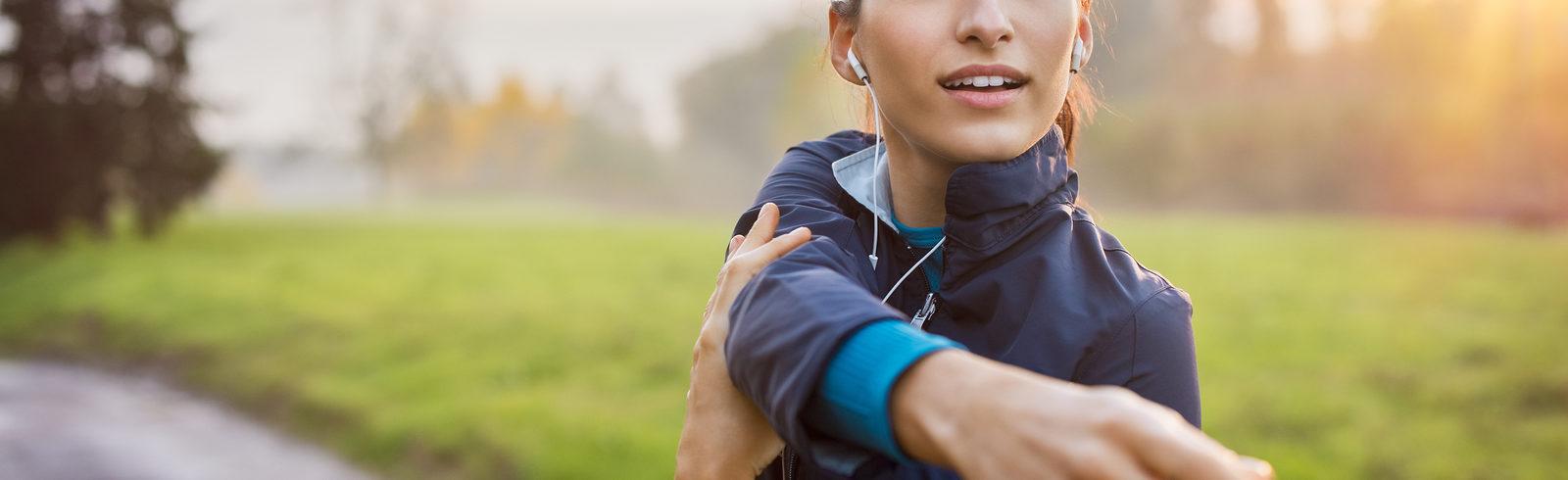 athletic person stretching their shoulder outside in a sunny park