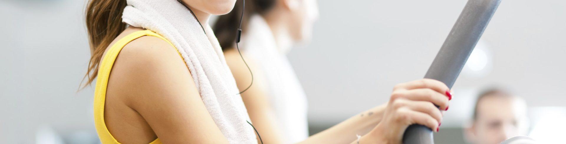 Smiling woman using an elliptical machine with a towel around her neck