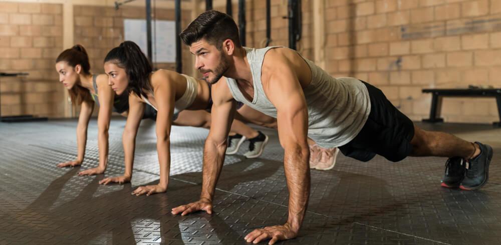 Confident young male and female athletes doing push-ups during cross training at gym