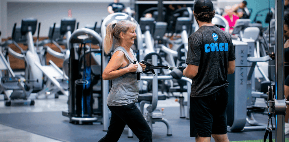 excited eos gym member performing a workout with personal trainer