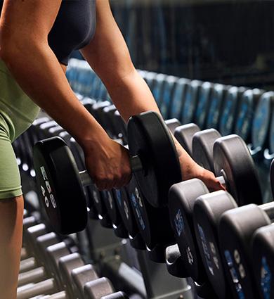 close up shot of eos gym member unracking a dumbbell from a large eos branded rack of weights