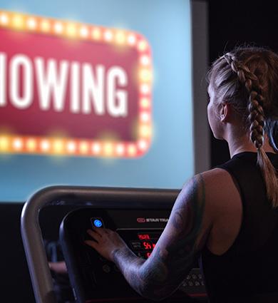 eos gym member on treadmill while watching a movie on a large screen