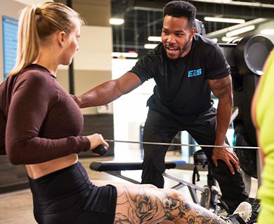 Personal trainer giving guidance to a woman on a rowing machine in a gym