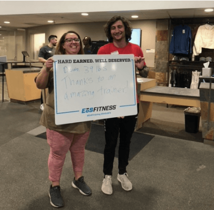 eos gym member standing side by side with personal trainer holding a white board listing how much weight they lost