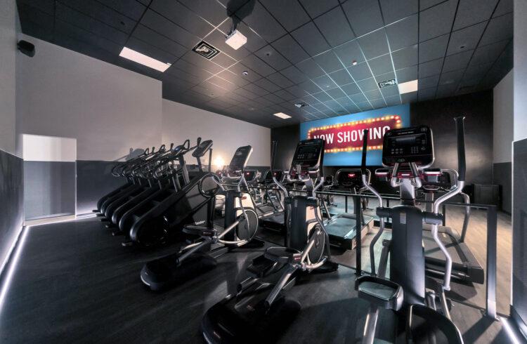 cinema room full of different cardio equipment and a large screen