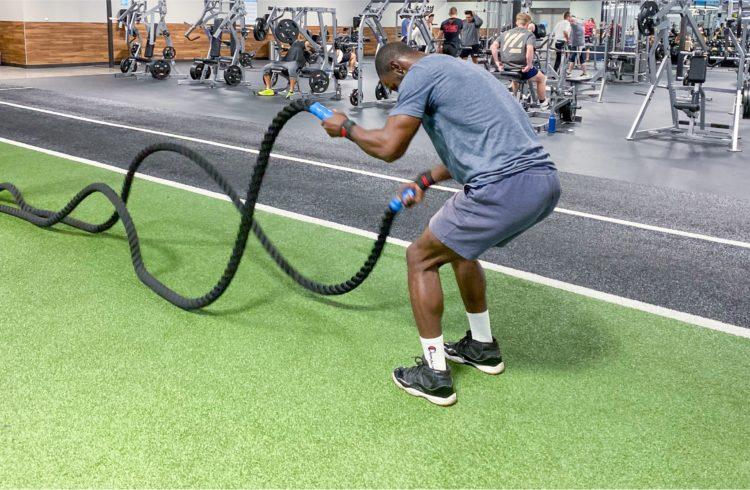 eos gym member working out with with battle ropes on turf