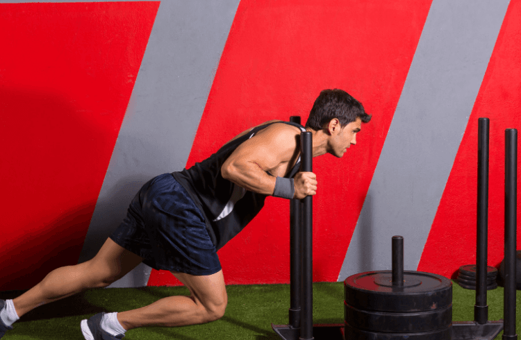 eos gym member pushing a sled on indoor turf