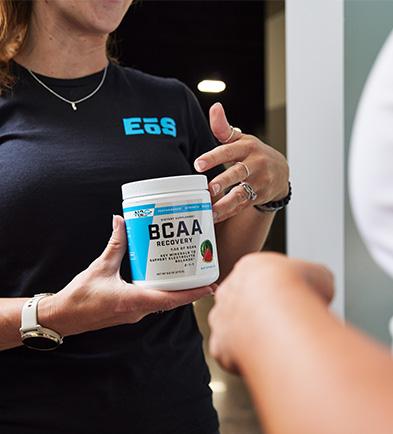 Close-up of a person holding a BCAA supplement container, with EoS branding on t-shirt.