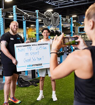 eos gym member side by side with personal trainer holding up white board indicating how much they lifted