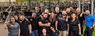 group shot of many eos staff members shoulder to shoulder smiling inside of a eos branded box gym