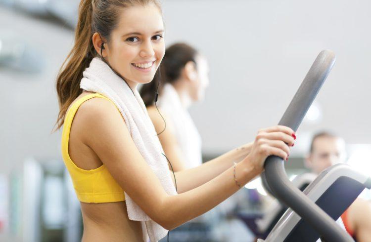 Smiling woman using an elliptical machine with a towel around her neck