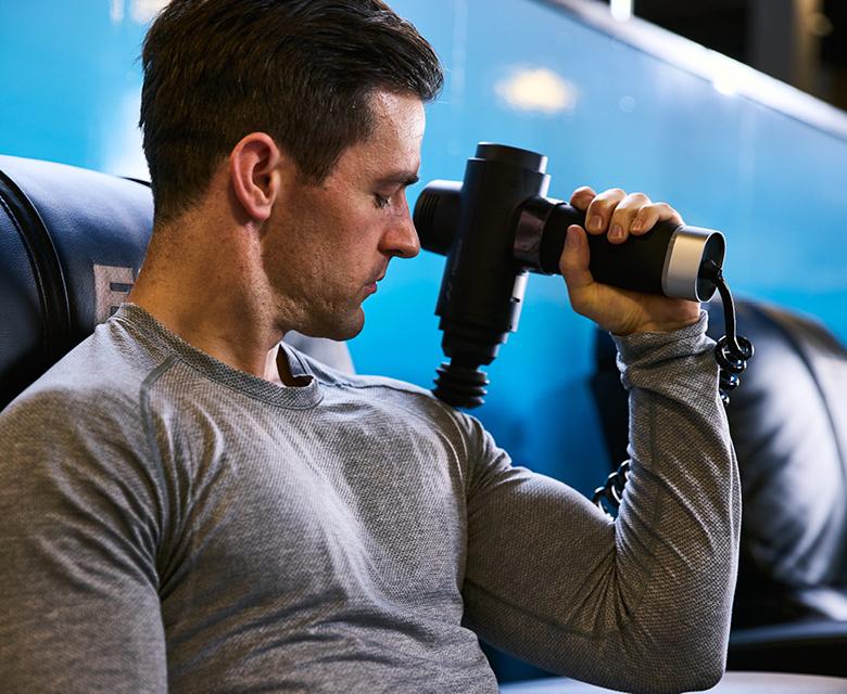 eos gym member using massager on their shoulder