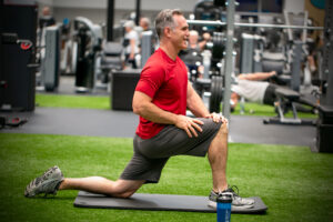 Man stretching his hip flexors on turf area in gym